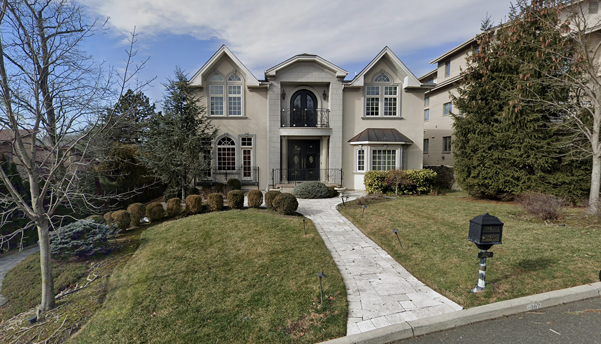 Two-story stucco colonial style house with arched windows, a stone walkway, manicured shrubs, and a front lawn mailbox